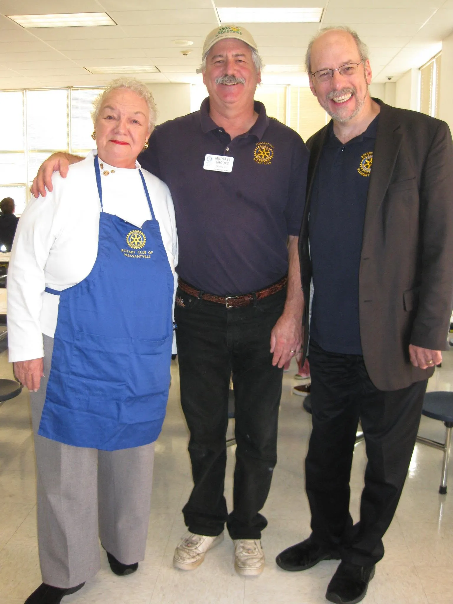 Helen Grishman in an apron with Mike Brooks and Pastor Paul at the Pancake Breakfast